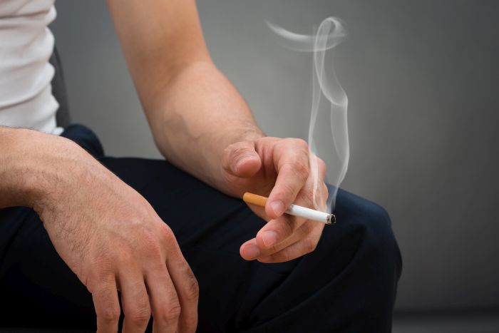 Midsection of man holding cigarette while sitting against gray background