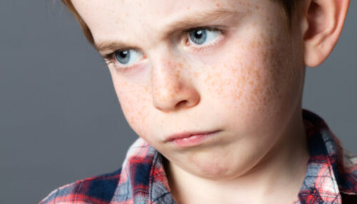 portrait of a disappointed little child with sad blue eyes and freckles for attitude and childhood resignation, grey background