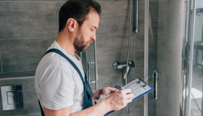 side view of male plumber making notes in clipboard while checking shower in bathroom